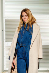 Portrait of happy beautiful young blonde woman in blue jeans and beige coat,