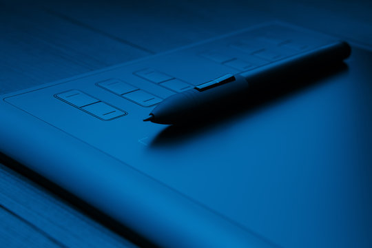 Graphic tablet with pen for illustrators and designers on black wooden background.