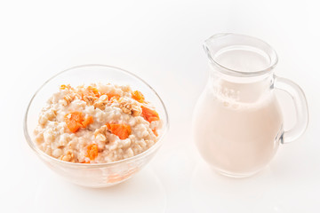 Oatmeal with pumpkin and nuts in a glass plate and a jug with milk on a white background. Close-up. Copy space