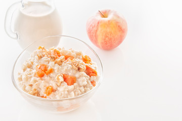 Oatmeal with pumpkin and nuts in a glass plate and a jug with milk on a white background. Close-up. Copy space