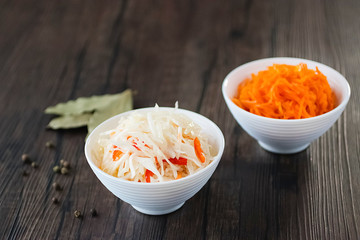 Marinated cabbage and carrots in white bowls on a brown wooden table. The concept of pickled and fermented vegetables.