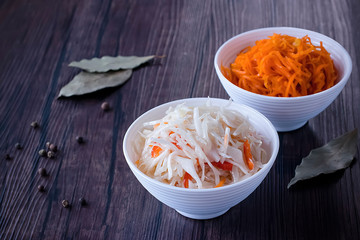 Marinated cabbage and carrots in white bowls on a brown wooden table. The concept of pickled and fermented vegetables.