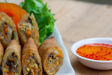 Deep fried spring rolls, Por Pieer Tod or Fried spring rolls (Thai Spring Roll) on white dish on wooden table,Thai and Chinese people.