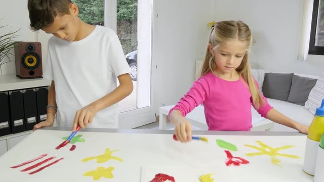 two beautiful young kids boy and girl painting on white paper with color paint