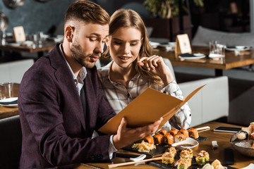 Beautiful young adult couple looking in menu to order dinner in restaurant