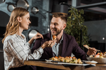Beautiful smiling young woman feeding her boyfriend with sushi in restaurant
