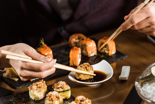 Cropped view of people eating sushi with chopsticks in restaurant
