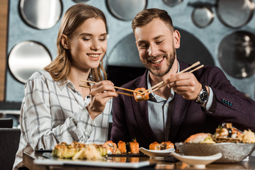 Smiling attractive young adult couple eating sushi together in restaurant
