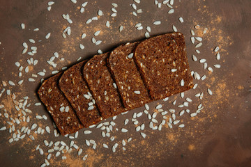 Sliced whole grain bread includes edible seeds such as poppy, millet, linseed, pumpkin seeds and sunflower seeds, on a brown background