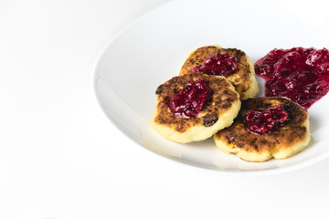 Fried cottage cheese pakcakes on a white plate. Syrniki with red jam on top.