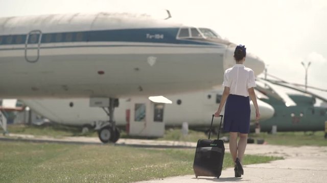 Beautiful and cheerful flight attendant walks towards the airplane.