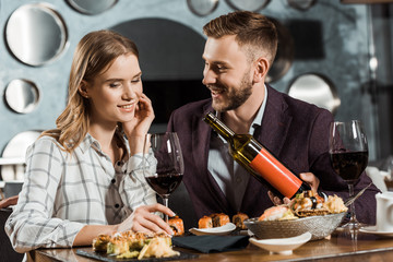 Handsome Man offering his beautiful girlfriend wine while they having dinner in restaurant