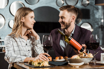 Handsome Man offering his girlfriend wine while they having dinner in restaurant