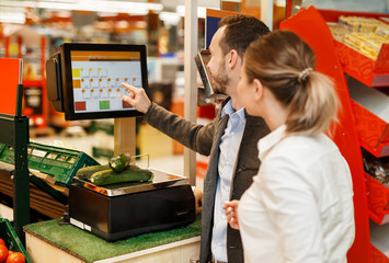 Couple is standing with fruit near weigher in supermarket