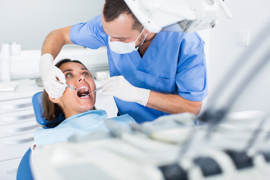 Dentist is treating patient which is sitting in dental chair in clinic