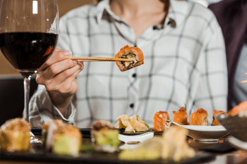 Partial view of woman eating sushi roll with chopsticks in restaurant