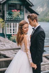 A beautiful wedding couple walks on the lake and mountains background in a fairy Austrian town, Hallstatt.