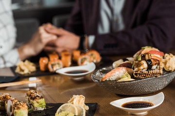 Sushi rolls and seafood on the background of couple holding hands