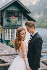 Naklejka premium A beautiful wedding couple walks on the lake and mountains background in a fairy Austrian town, Hallstatt.