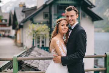 Fototapeta premium A beautiful wedding couple walks on the lake and mountains background in a fairy Austrian town, Hallstatt.