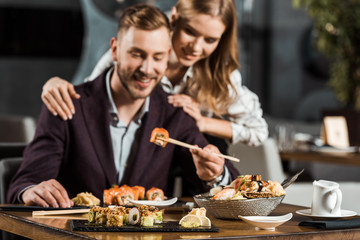 Happy attractive couple having dinner and eating tasty sushi rolls in restaurant