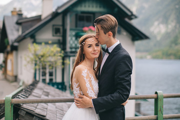 A beautiful wedding couple walks on the lake and mountains background in a fairy Austrian town, Hallstatt.
