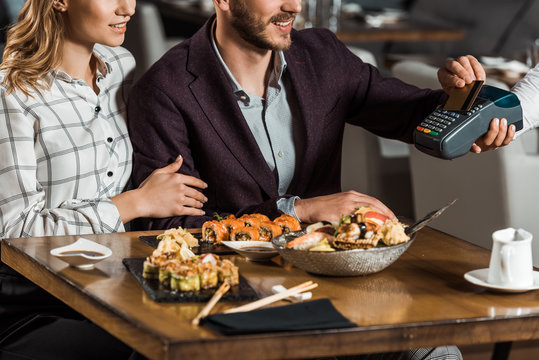 Partial View Of Couple Sitting At Table While Man Paying For Dinner In Restaurant