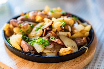 Roasted potato in frying pan with meat and green leek
