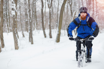 Fototapeta na wymiar Focused young man with long beard riding a mountain bike through deep powder snow in a forest. Active sport lifestyle in cold weather.