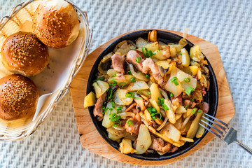 Roasted potato in frying pan with meat and green leek