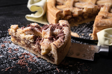 Apple pie slice on a knife with sugar and chocolate. Close-up. Ready to eat.