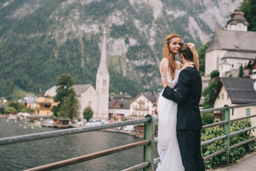 A beautiful wedding couple walks on a background old cathedral, lake and mountains in a fairy Austrian town, Hallstatt.
