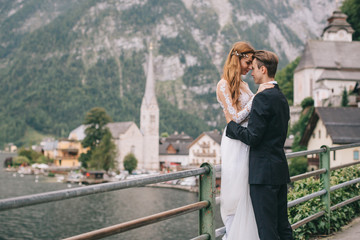 A beautiful wedding couple walks on a background old cathedral, lake and mountains in a fairy Austrian town, Hallstatt.