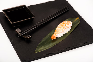 Nigiri sushi with shrimp served with chopsticks and soy sauce on black slate