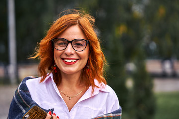 Portrait of a beautiful smiling middle-aged woman with red hair wearing glasses on a cloudy day....