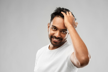 grooming and people concept - smiling young indian man touching his hair over gray background