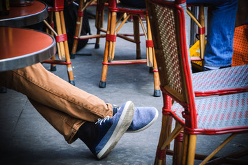 Man's legs in in gumshoes. Tourists sitting traditional outdoor Parisian cafe. Toned image. - Powered by Adobe