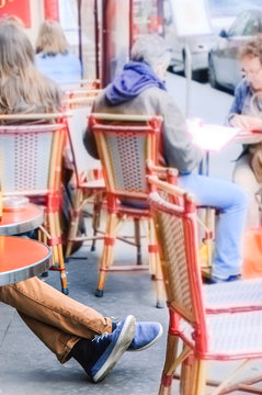 Man's legs in in gumshoes. Tourists sitting traditional outdoor Parisian cafe. Blurred unrecognizable people at background. Toned image.