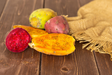Group of one whole four halves of fresh bright prickly pear opuntia on jute cloth on brown wood