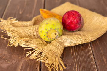 Group of one whole two halves of fresh bright prickly pear opuntia on jute cloth on brown wood
