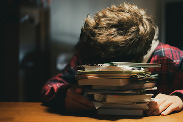 tired teenage pupil lying on the table doing homework late in the night f