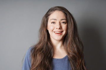 Obraz premium happy young woman in her 20s with natural make-up and brunette long hair smiling toothy smile - against gray background with copy space