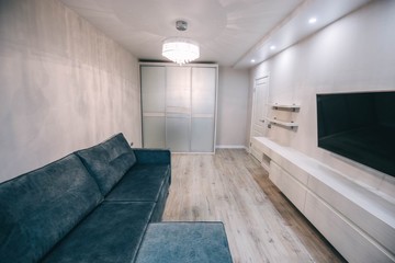  Interior of a modern small room with a green-blue sofa, a TV, a chandelier.