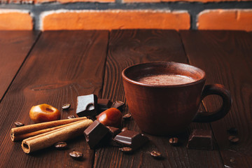 Hot chocolate drink in a brown clay cup, chocolate cubes, cinnamon sticks and coffee bean on the...
