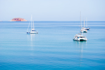 Two catamarans and three sailboats anchored in the middle of the sea