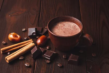 Fotobehang Hot chocolate drink in a brown clay cup, chocolate cubes, cinnamon sticks and coffee bean on the dark wooden background © O.Farion