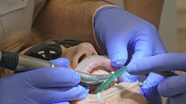 Dentist is treating a patient in a modern dental office. Orthodontist works with an assistant. The operation is carried out using a cofferdam. The client is inserted and restored teeth, make a denture