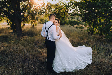 A young bridegroom embraces a beautiful bride at sunset, in sunny weather. Happy newlyweds are...