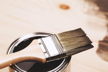 Paintbrush and a newly opened can of grey paint on wooden surface