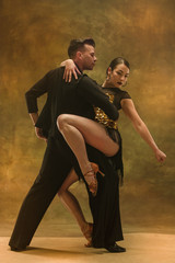 The young dance ballroom couple in gold dress dancing in sensual pose on studio background. Professional dancers dancing tango. Ballroom dance concept. Human emotions - love and passion